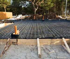 Iron fittings on a wooden blind area with laid pipes are the basis for pouring the foundation of the house with a concrete slab. Construction of cottages, design, engineering communications.