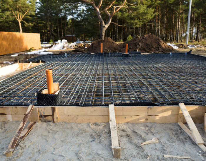 Iron fittings on a wooden blind area with laid pipes are the basis for pouring the foundation of the house with a concrete slab. Construction of cottages, design, engineering communications.