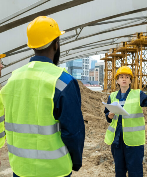 Group of engineers standing on the site and discussing the work of future project in team